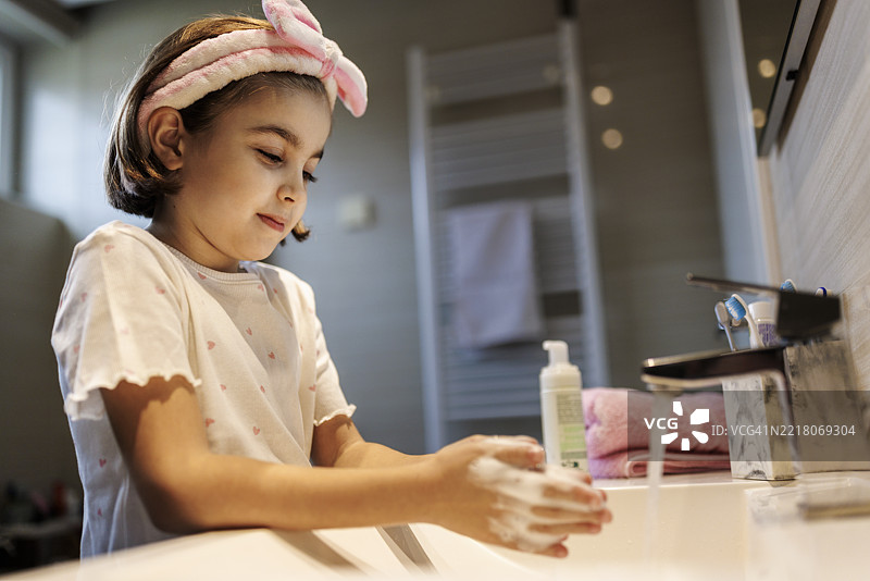 可爱的小女孩戴着毛茸茸的粉色头带在洗手图片素材