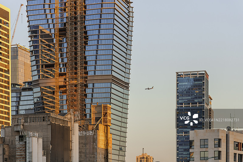 现代高楼在日落时分建设中，天空中有一架飞机。图片素材