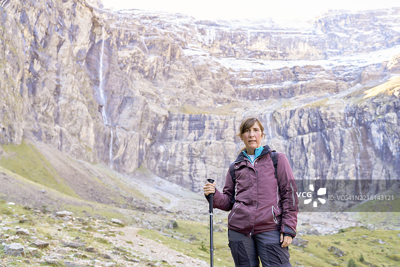 在山中徒步旅行的女性手持登山杖，站在瀑布前摆姿势图片素材
