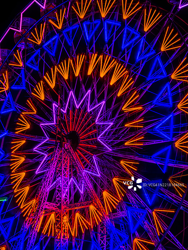 一个充满活力的摩天轮在夜晚的地方集市上被霓虹灯照亮,位于印度马哈拉施特拉邦纳维孟买附近的一个村庄。图像捕捉了传统节日的活力和色彩,带有现代的风格。图片素材