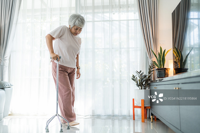 老年女性在客厅里拄着手杖走路图片素材