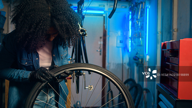 年轻的机械师在霓虹灯照亮的车间修理自行车轮子图片素材