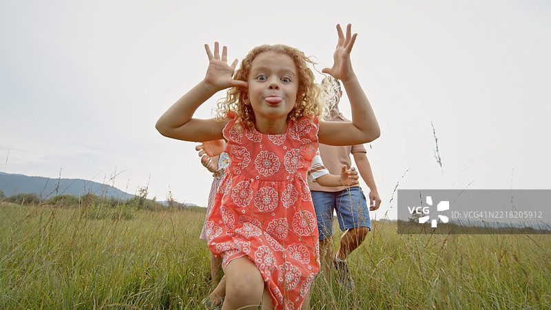 快乐的金发女孩穿着红色裙子，在日落时分的草地上与家人一起玩耍。图片素材