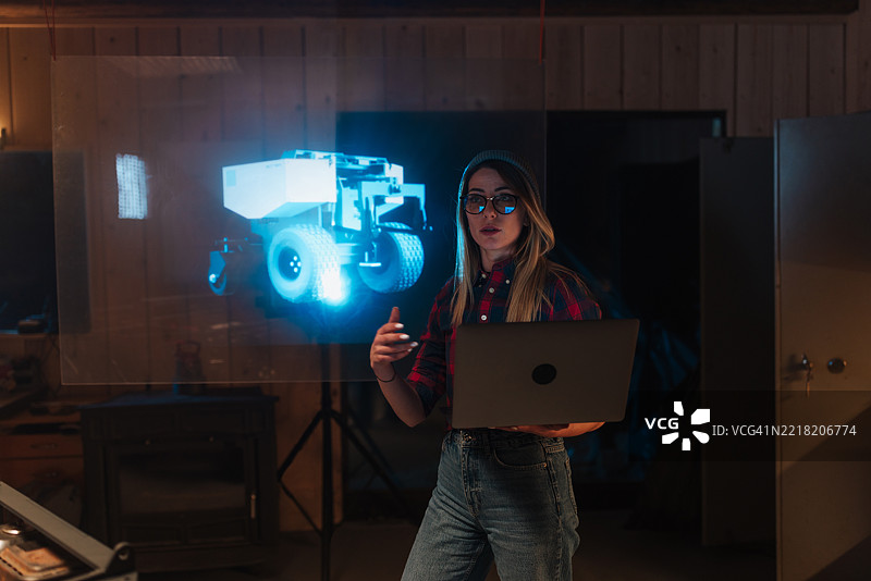 工程师正在使用未来派透明全息屏幕和笔记本电脑，开发机器人车辆图片素材
