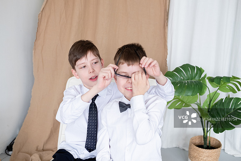 两个11岁和12岁的兄弟穿着白衬衫和领结，在拍照时开心地跳舞。一个戴着助听器和眼镜的孩子在家庭生活中。图片素材