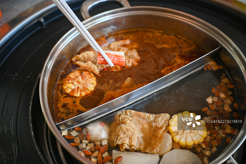 一位女性用筷子夹着海鲜，靠近不锈钢火锅的特写照片图片素材