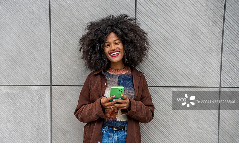 年轻女性在灰色墙壁旁使用手机并微笑图片素材
