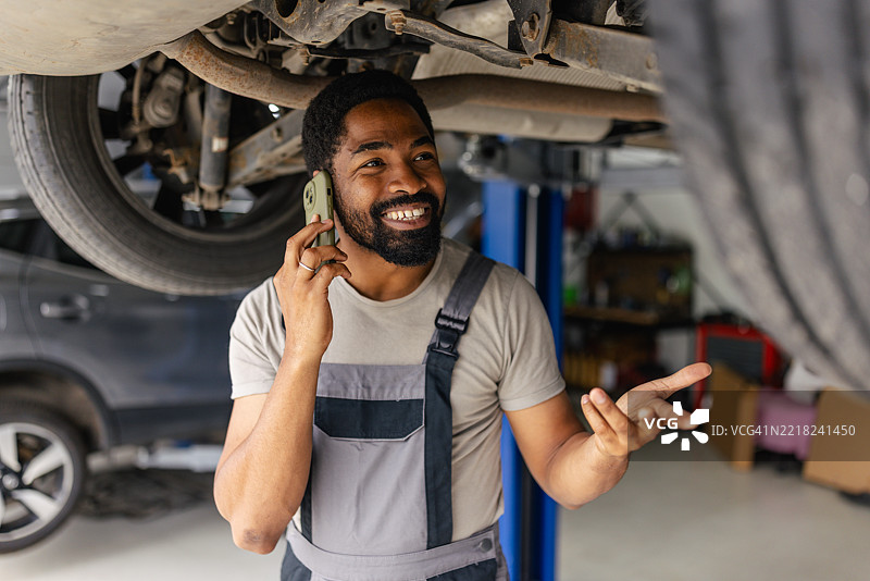 微笑的机械师在车辆下使用手机图片素材