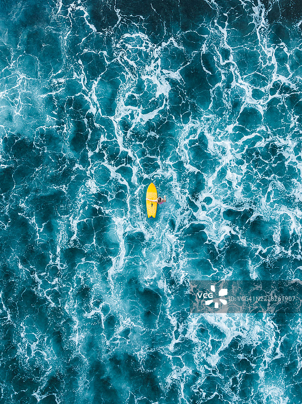 一位女性站在一块黄色冲浪板旁,背景是印度洋,从无人机视角拍摄,地点为印尼巴厘岛乌鲁瓦图。图片素材