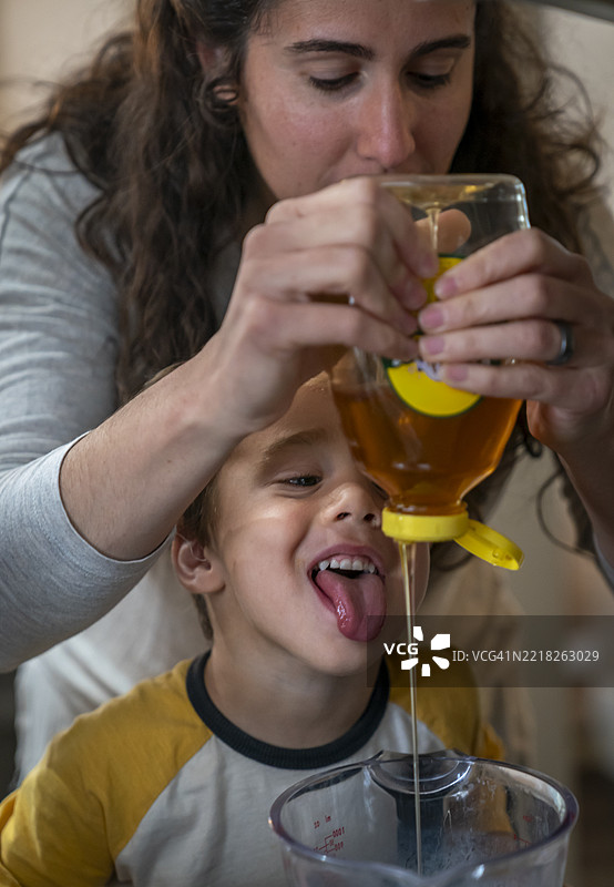 母亲和4岁男孩正在将蜂蜜倒入玻璃量杯中图片素材