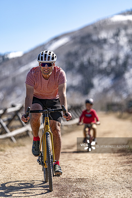 拉丁裔父亲骑着山地自行车在卵石小径上，4岁的儿子坐在后面。图片素材