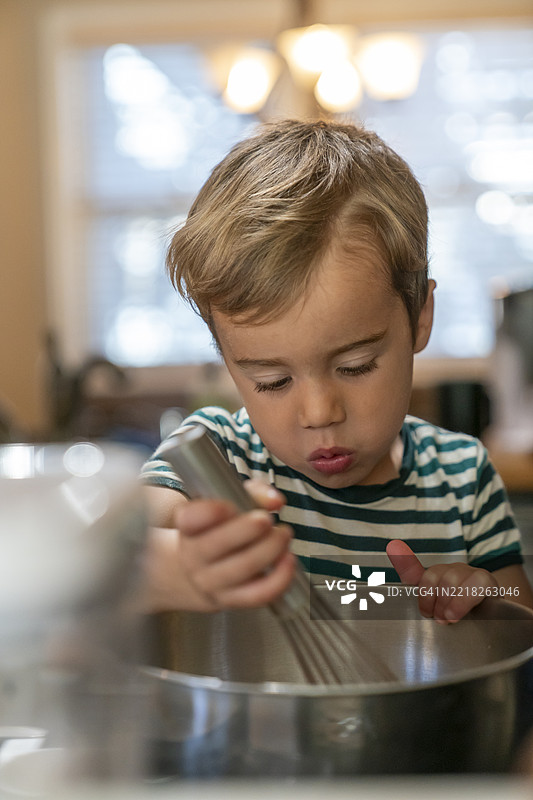 4岁男孩用打蛋器在金属碗中搅拌糕点面糊图片素材