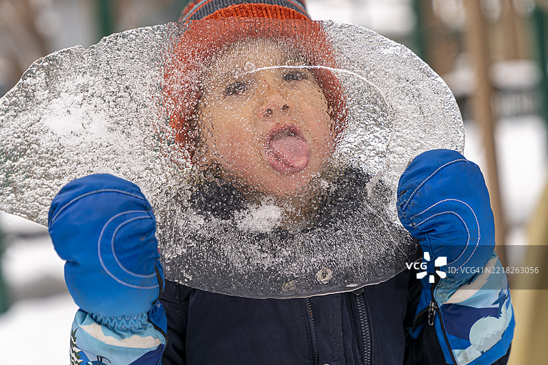 4岁男孩戴着冬季手套舔着手中的大冰块图片素材