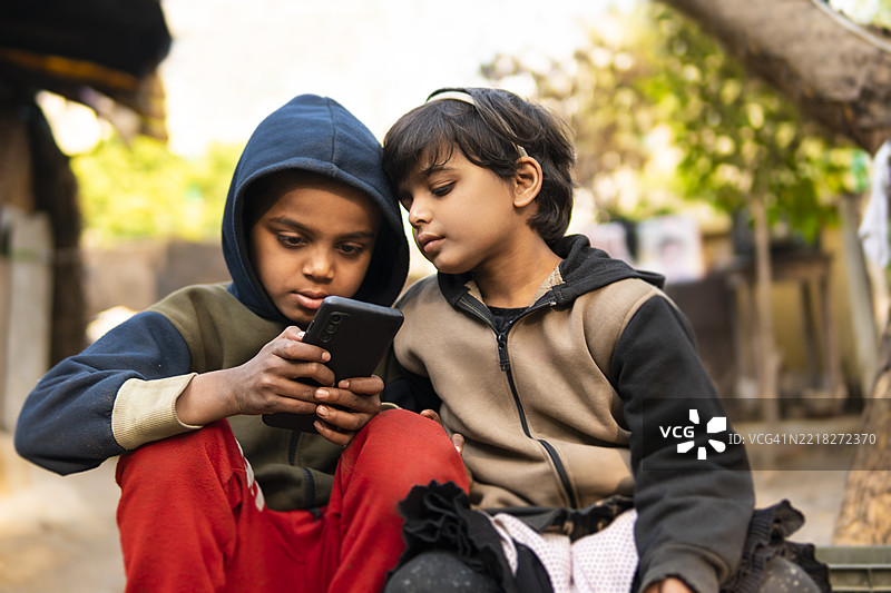 两个快乐的印度乡村兄妹一起玩耍并使用智能手机。图片素材