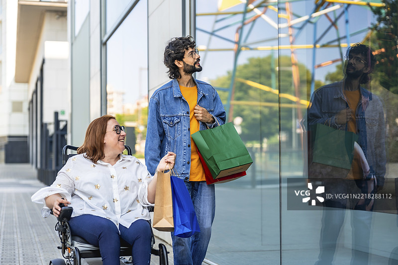 微笑的情侣提着购物袋走过商店橱窗，享受着一起购物的美好时光图片素材
