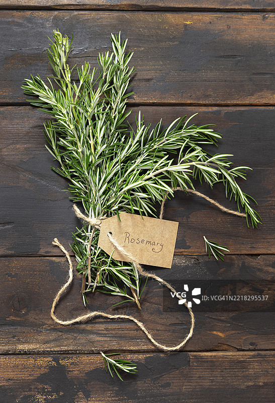 新鲜的绿色迷迭香枝条，带有牛皮纸标签，放在深色老旧木桌上俯视图图片素材