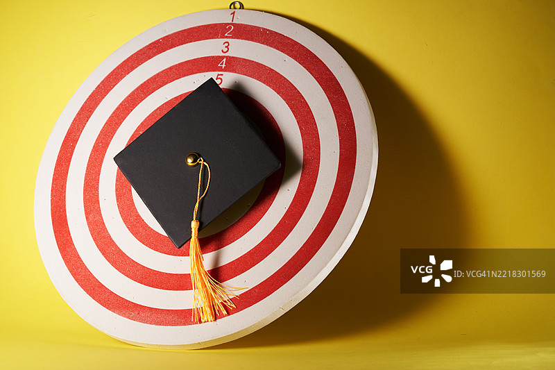 黄背景上的靶心上放着学位帽。图片素材