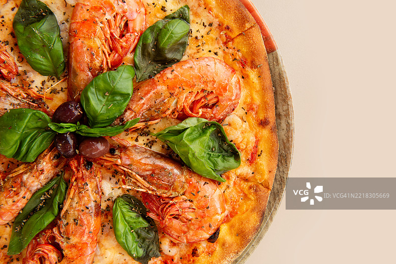 美味的披萨，上面有虾、马苏里拉奶酪、罗勒和黑橄榄，摆放在盘子里图片素材
