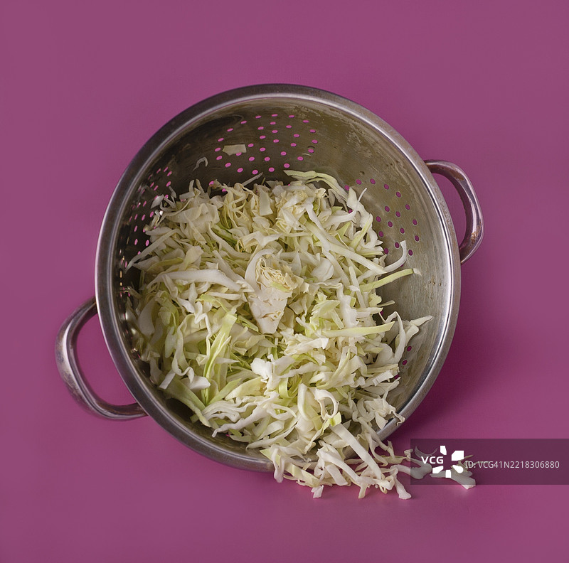 紫色背景上的切碎白卷心菜放在漏网中图片素材