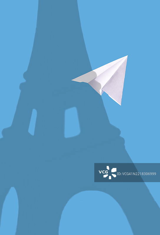 一张白色的纸飞机在蓝色背景上飞行，埃菲尔铁塔的影子图片素材