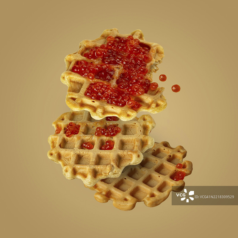 自制维也纳华夫饼配红鱼子酱，背景为黄色，飞舞的食物图片素材