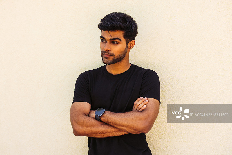 自信的年轻男子双臂交叉，穿着休闲服装，目光远眺。图片素材