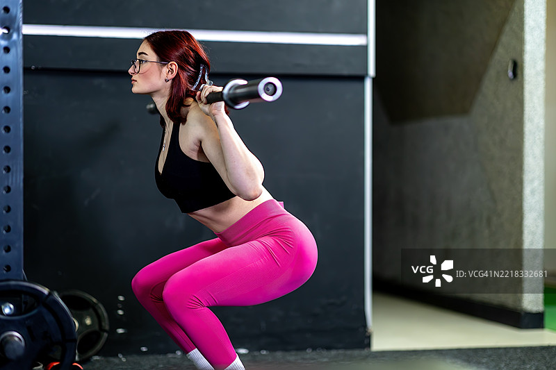 在现代健身房环境中进行负重深蹲的运动女性图片素材