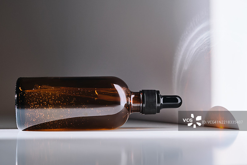 一瓶棕色玻璃制成的精华液，背景为白色，带有光线条纹。图片素材