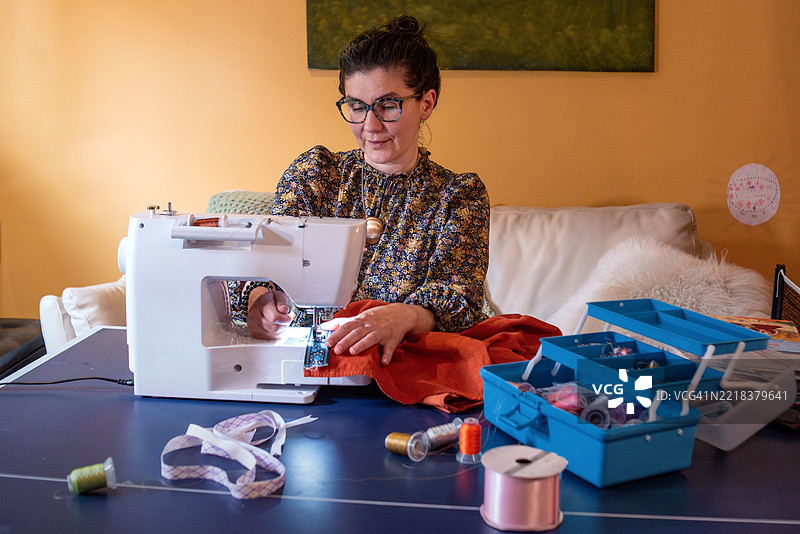 棕发女性使用白色缝纫机在红色面料上工作。图片素材