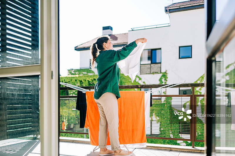 阳光明媚的日子，女人在阳台上晾晒衣物图片素材