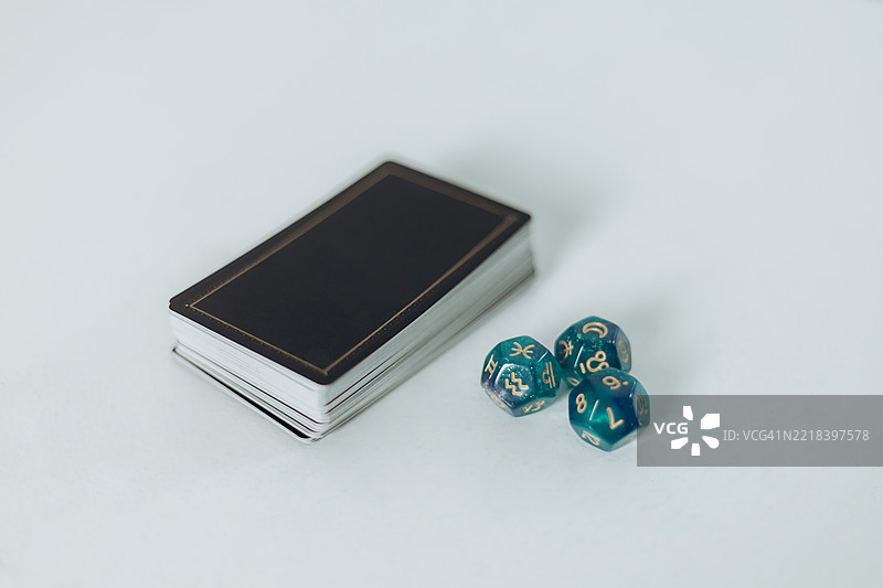 一副黑色扑克牌和一个12面骰子放在白色表面上。图片素材