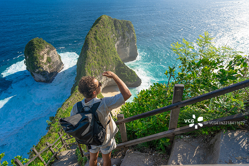 男性游客在印度尼西亚努沙佩尼达岛的凯灵金海滩游玩。攀爬台阶小径到达顶部。图片素材