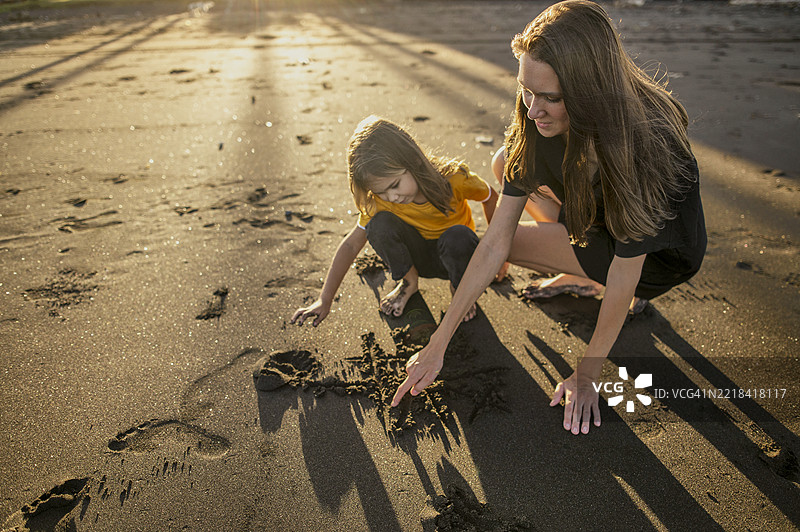 母女在海滩上用沙子画画图片素材
