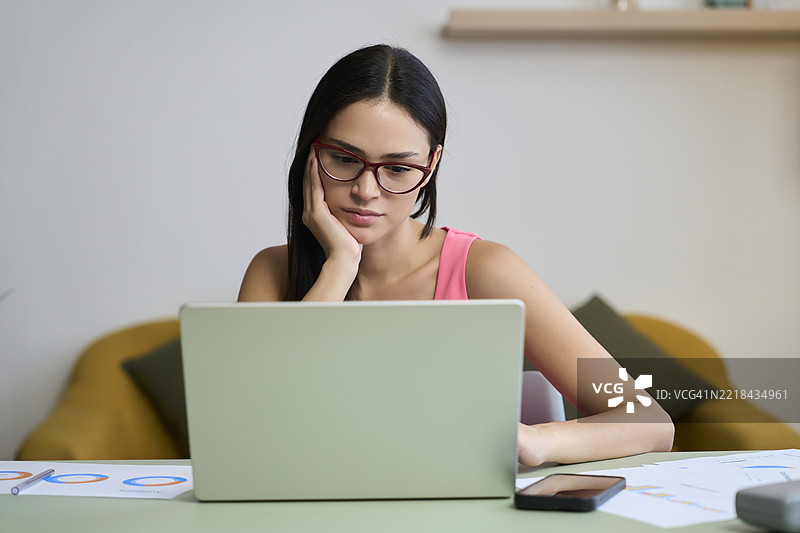 专注的年轻女性在家用笔记本电脑工作图片素材