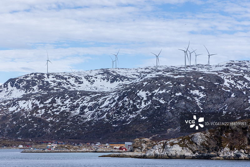 雄伟的风力涡轮机矗立在雪山山脊上，俯瞰着海滨村庄图片素材