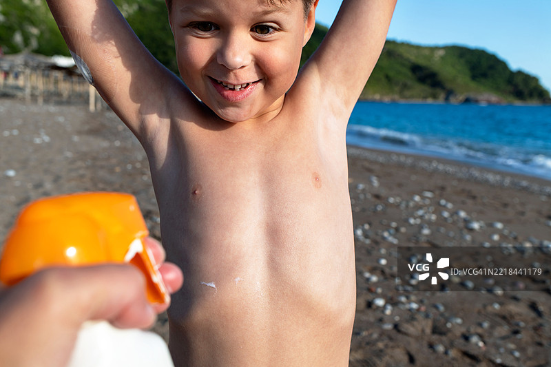 一个手上戴着血糖传感器的孩子在海滩上涂抹防晒霜，享受阳光。图片素材