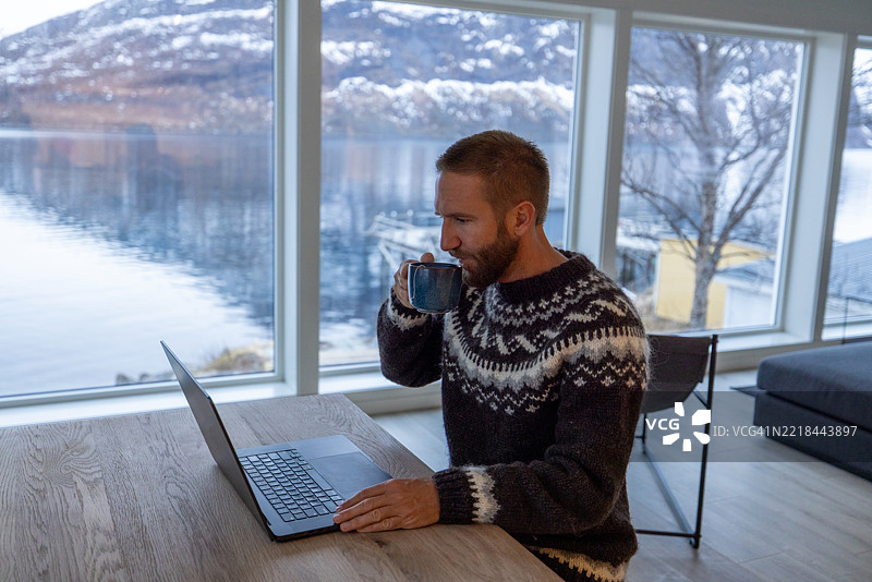 穿着北欧毛衣的男子在家办公室进行视频通话，背景是美丽的风景图片素材