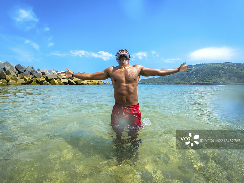 游客在热带天堂的清澈海水中张开双臂，拥抱自由，享受阳光的温暖和宁静。图片素材