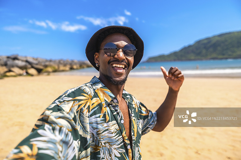 年轻男子在热带海滩享受暑假，微笑着自拍并竖起大拇指，洋溢着快乐。图片素材