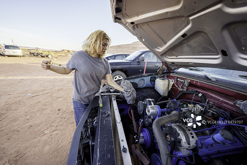 漂亮的纳瓦霍少女在亚利桑那州的纪念谷沙漠地区，阳光明媚的日子里，打开车盖检查发动机油。图片素材