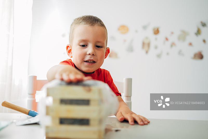 男孩用塑料膜覆盖窗台上的草莓幼苗容器，为家庭花园做准备。图片素材