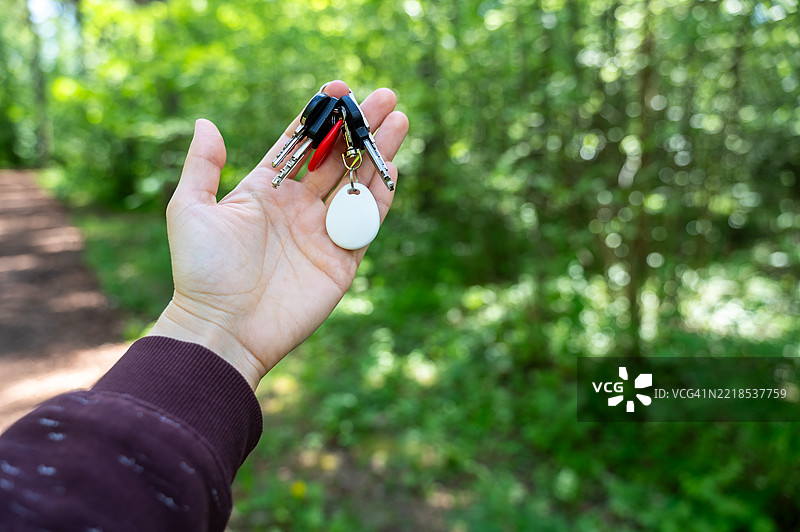 手握带有GPS追踪器钥匙链的钥匙在森林中图片素材