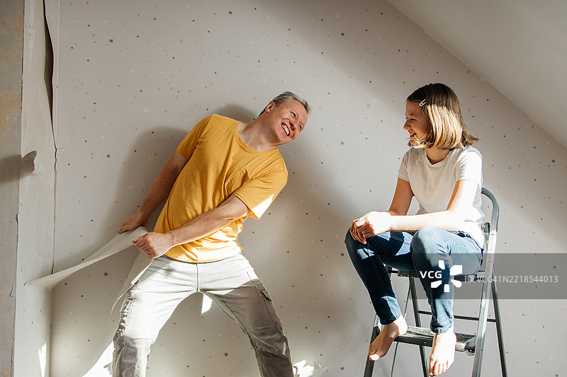 一位父亲和他的 teenage 女儿正在为儿童房的装修做准备，撕掉墙纸。孩子们在帮助他们的父母。图片素材