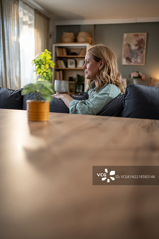 女人在沙发上放松，手握热饮，享受在家中的宁静时光图片素材