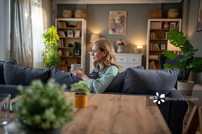 宁静的女人在家中的沙发上享受安静的咖啡时光图片素材