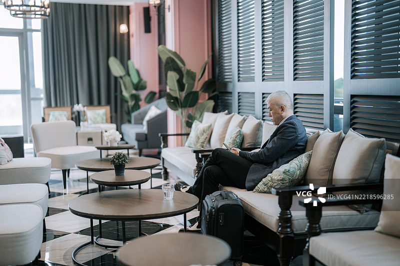 亚洲老年商人在酒店休息室等待，身边有行李图片素材