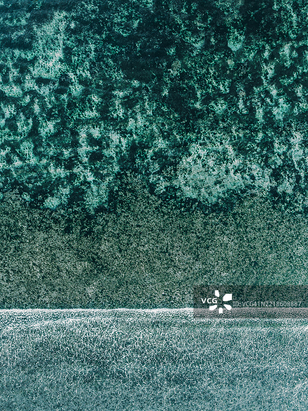 从无人机视角拍摄的印尼巴厘岛乌鲁瓦图海岸附近的海浪朝向礁石涌来。图片素材