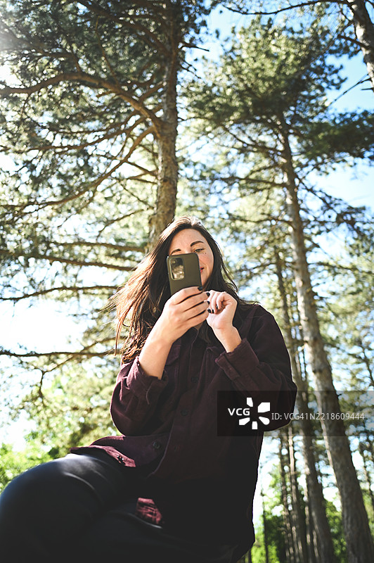 年轻女性在阳光明媚的日子里在森林中使用智能手机图片素材