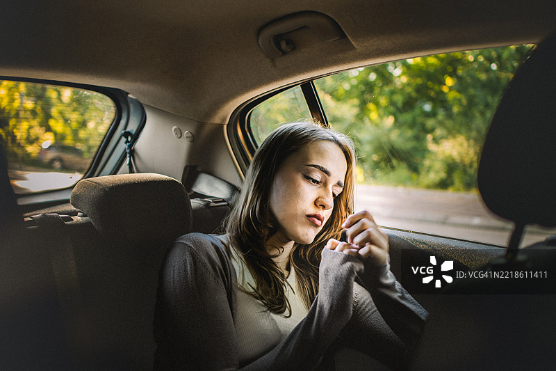 一位美丽年轻女性坐在车后座上，感到悲伤、无助和沮丧。图片素材