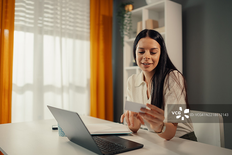 年轻女性在家工作，视频通话时阅读名片图片素材